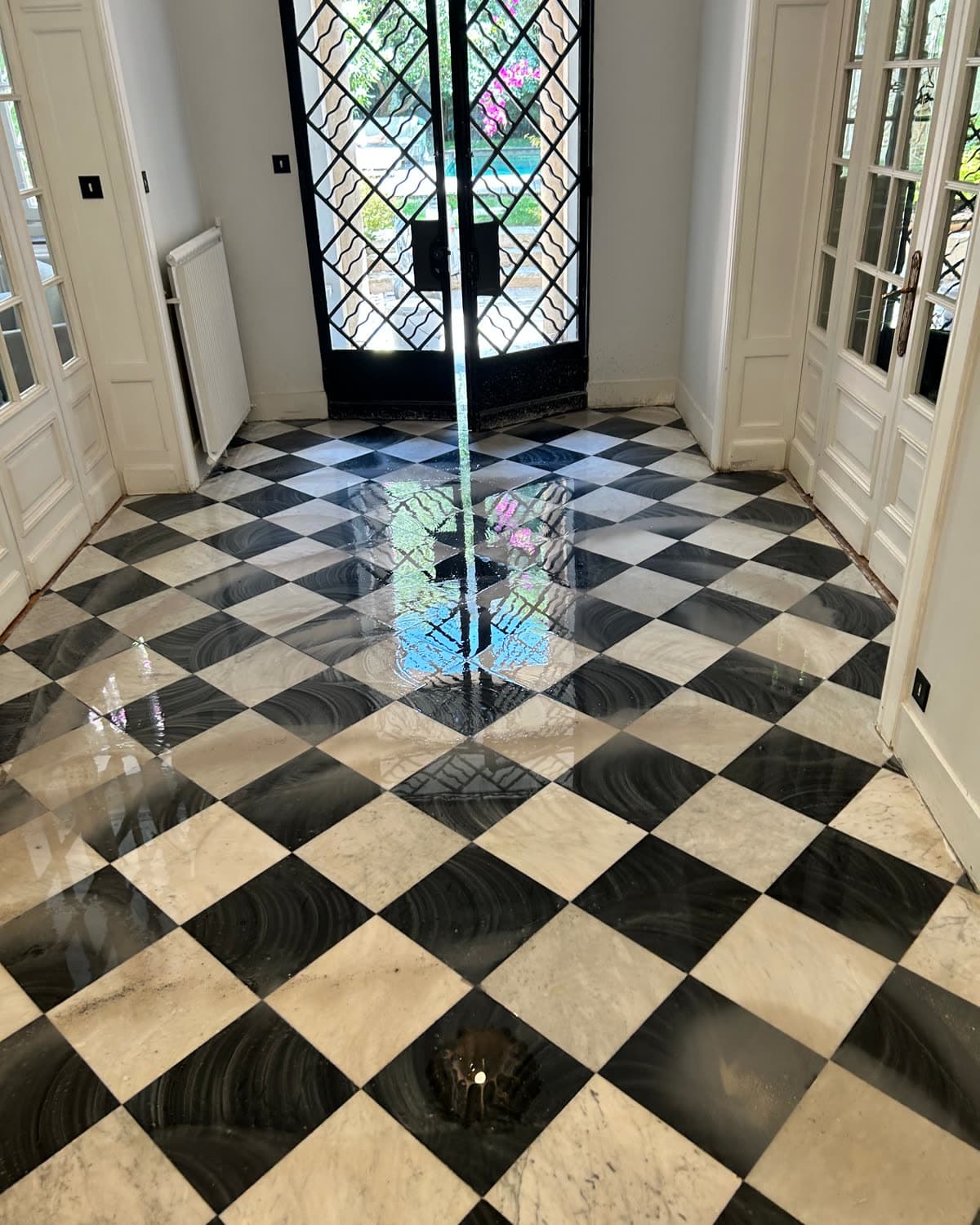 Hall d'entrée en damier de marbre noir et blanc après cristallisation, la porte en fer forgé se reflète dans le sol.