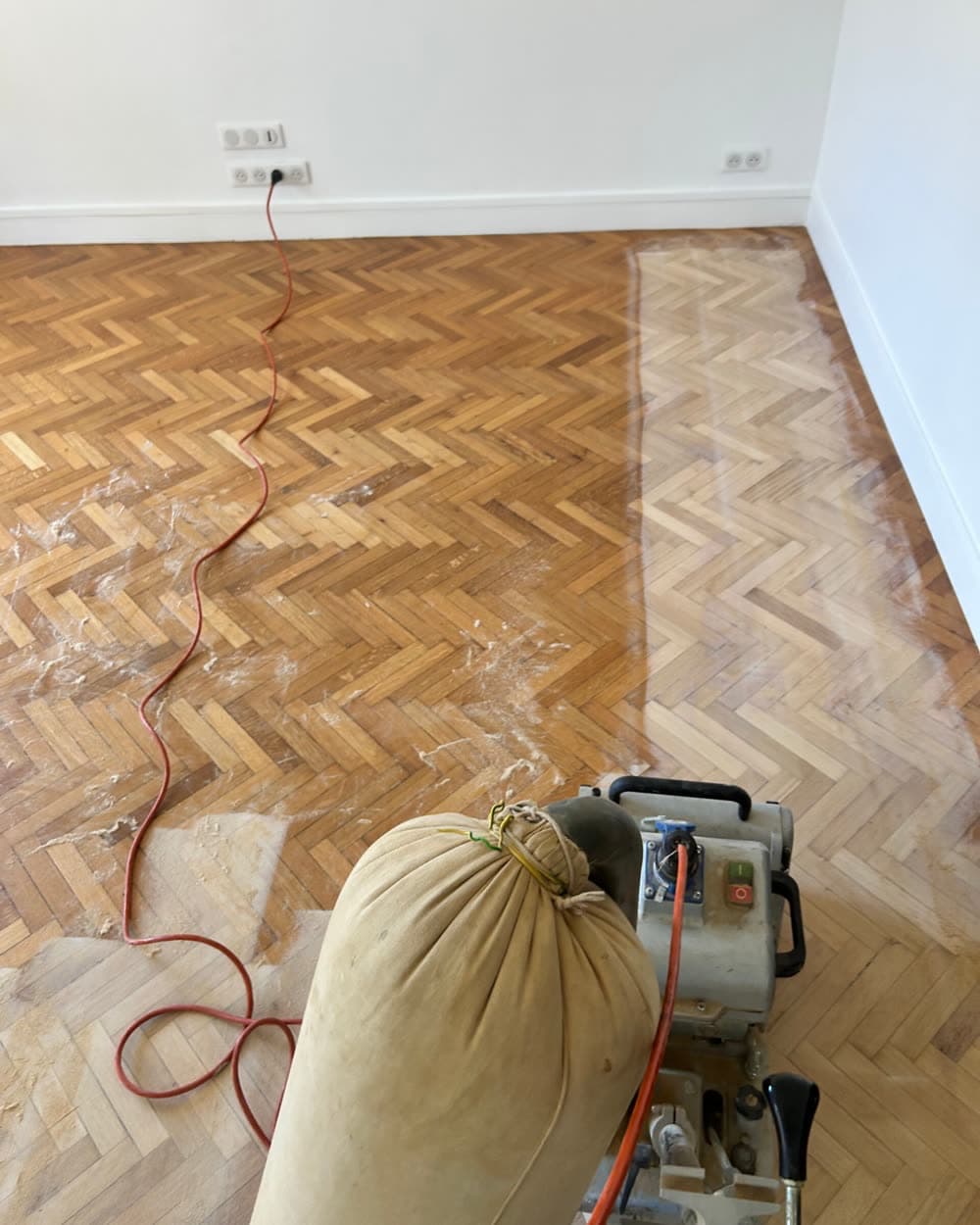 Parquet point de Hongrie à moitié poncé, la ponceuse dans le cadre.