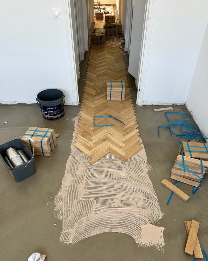 Pose de parquet point de Hongrie en cours dans un couloir, colle et lames scotchées.